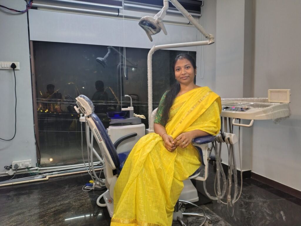 Dr. Divyashree Venkatesan, dentist, sitting and smiling in front of a modern dental chair at Dentick Dental Care, JP Nagar branch near Puttenahalli Lake, Bangalore.